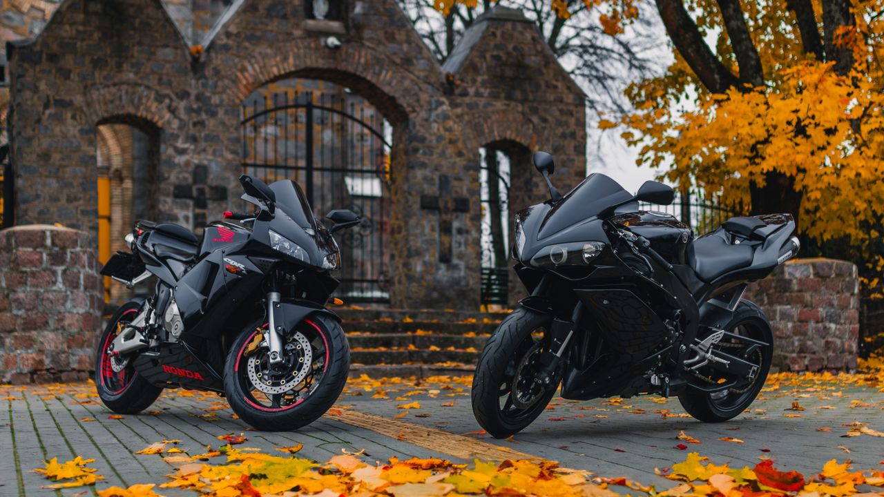 Two sport motorcycles parked in front of a stone church during fall with vibrant leaves.